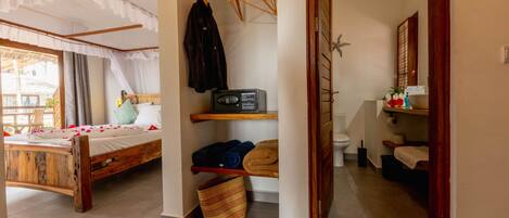 Quarto com cama de madeira, uma prateleira pequena com roupas dobradas, um rádio e um cesto.
