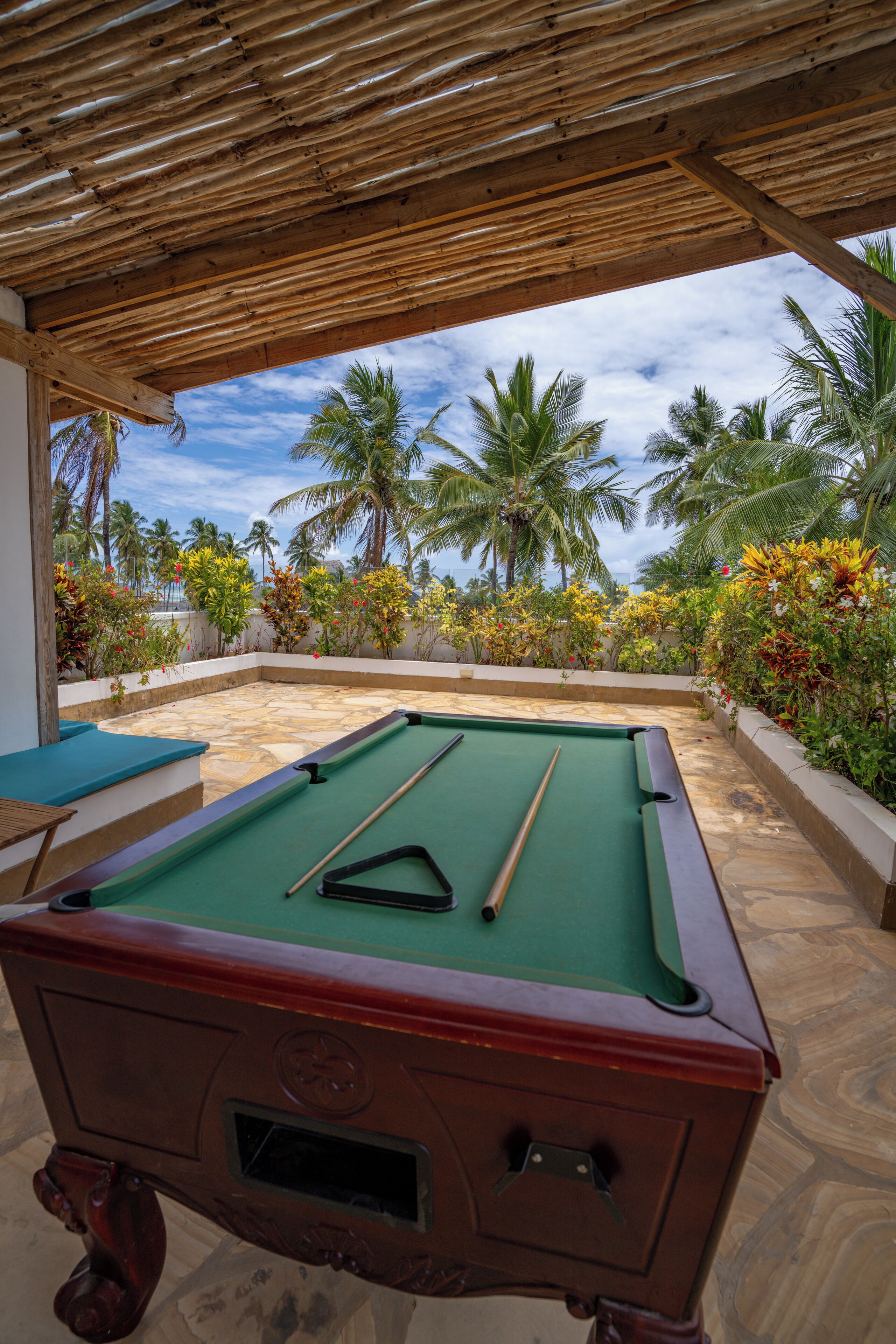 Área externa com piscina, teto de madeira, mesa de bilhar e plantas tropicais ao redor.