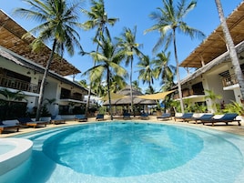 A pool area with lounge chairs, palm trees, and a thatched-roof structure.