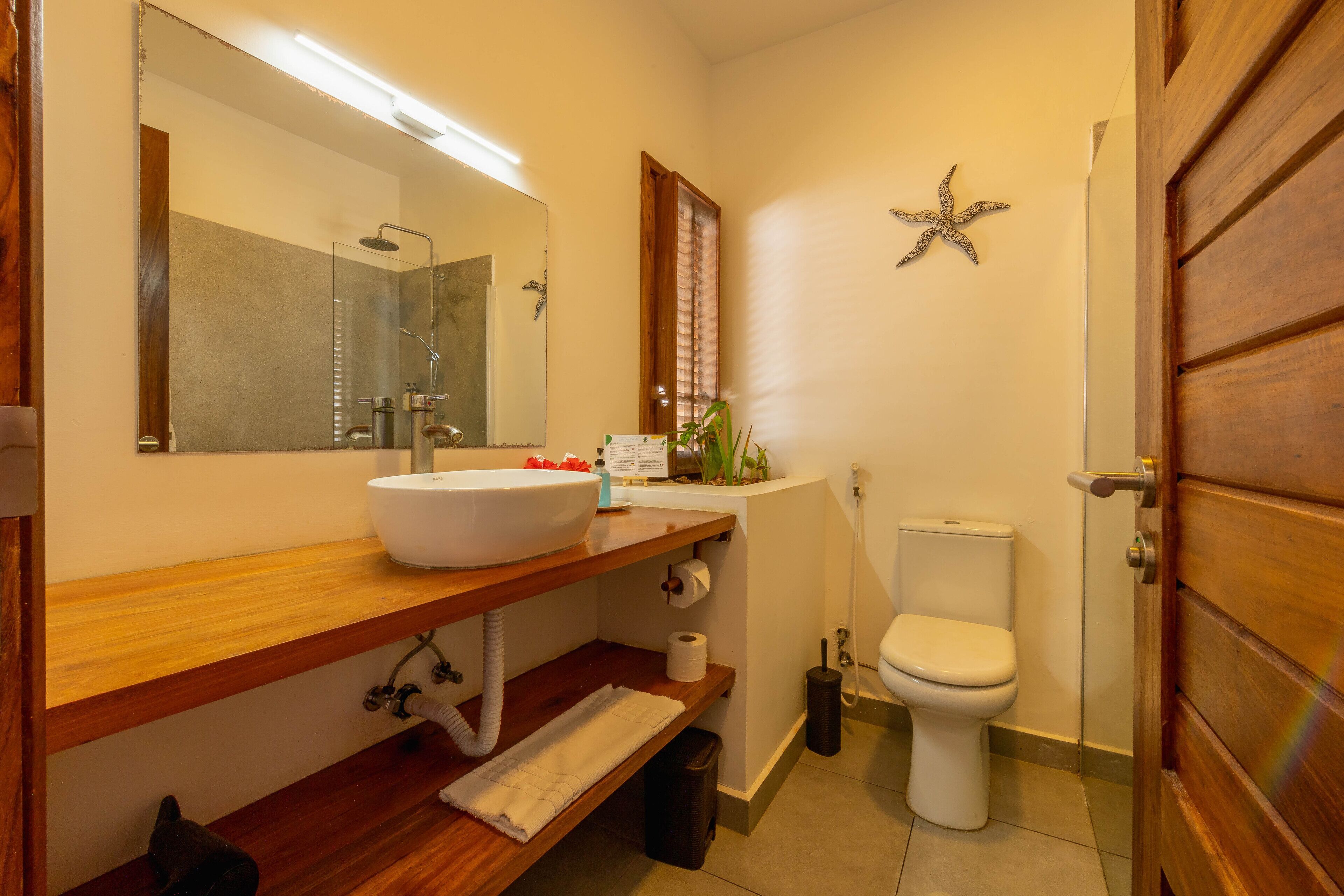 Een badkamer met een houten wastafelmeubel, een witte wasbak, een spiegel, een toilet en een douche.