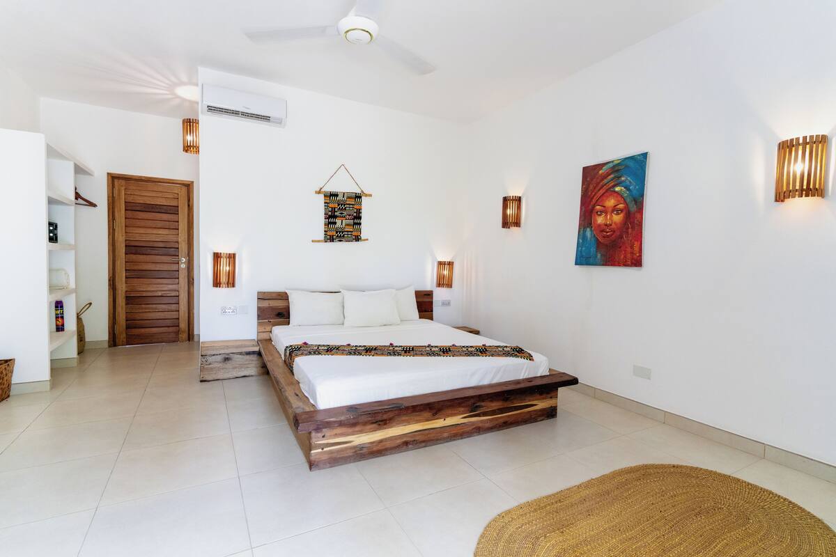 Ein Schlafzimmer mit hölzernem Bettgestell, weißer Bettwäsche, Deckenventilator, Wandleuchten und einem Gemälde.
