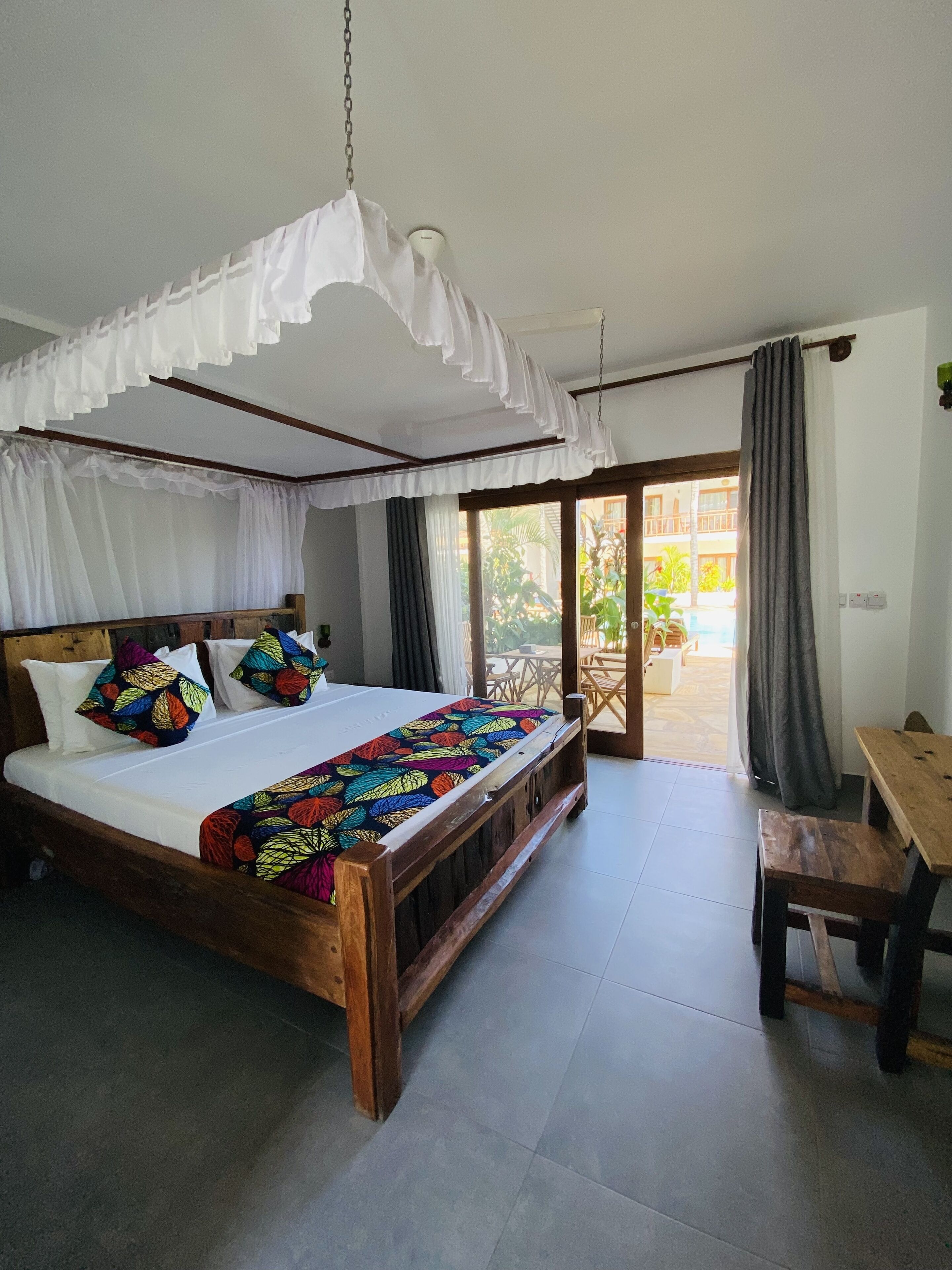 Un dormitorio con una cama de madera, almohadas coloridas, un dosel y vistas al exterior.