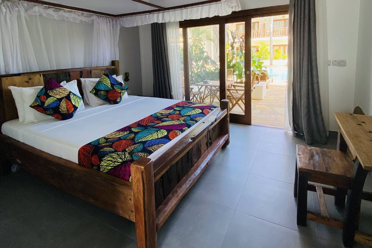 Ein Schlafzimmer mit einem Holzbett, bunten Kissen, einem Baldachin und Blick ins Freie.