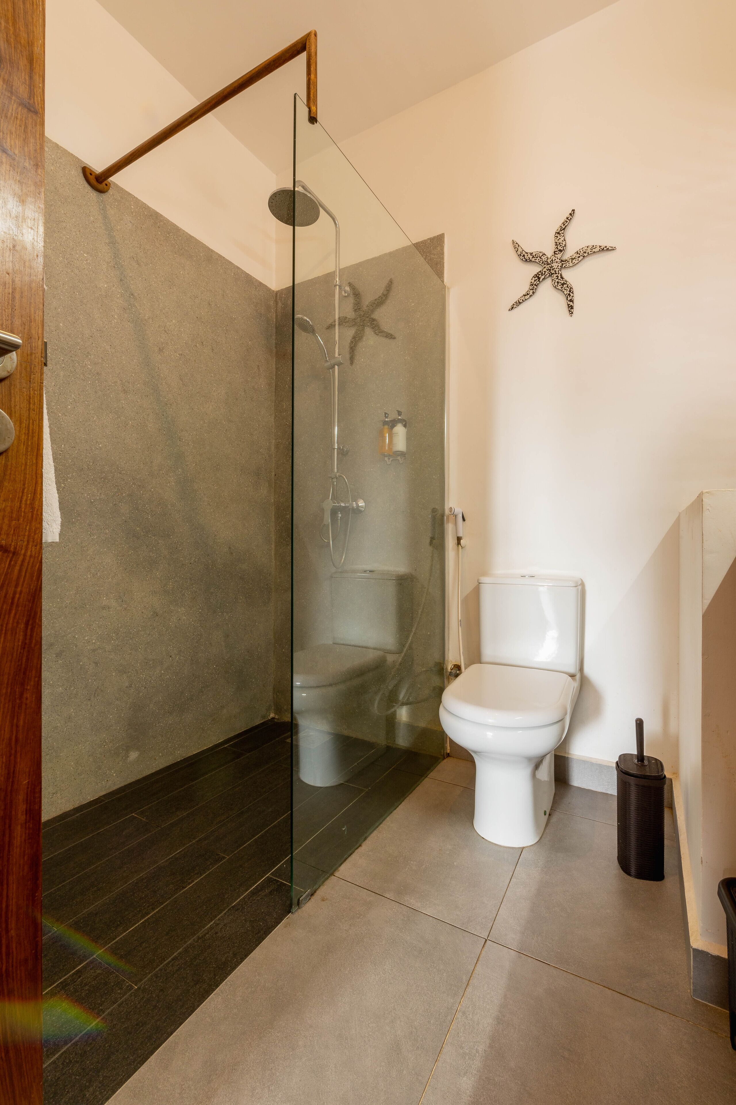 A modern bathroom with a glass-enclosed shower, a white toilet, and a starfish decoration on the wall.