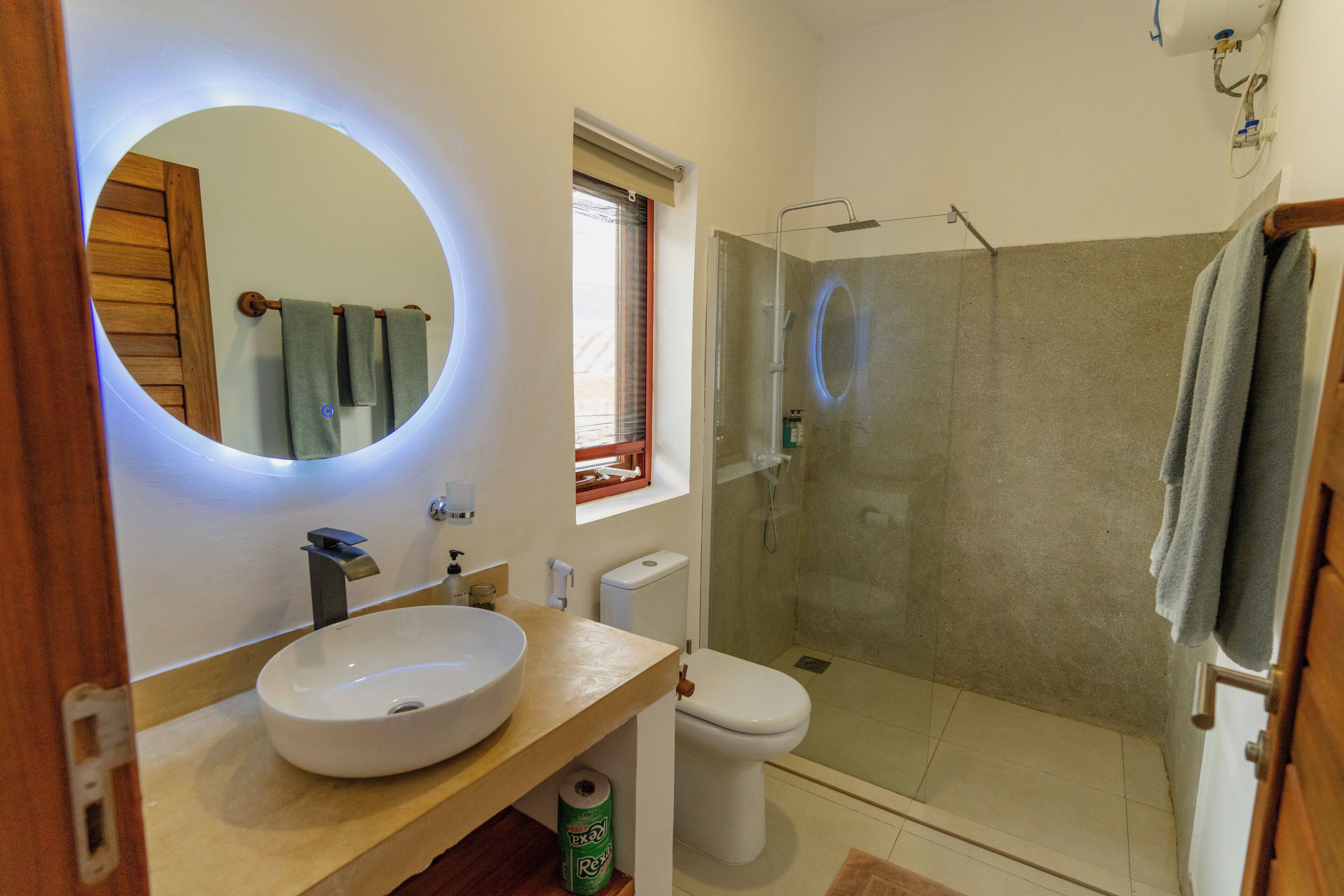 A bathroom with a round mirror, a sink, a toilet, and a glass-enclosed shower.