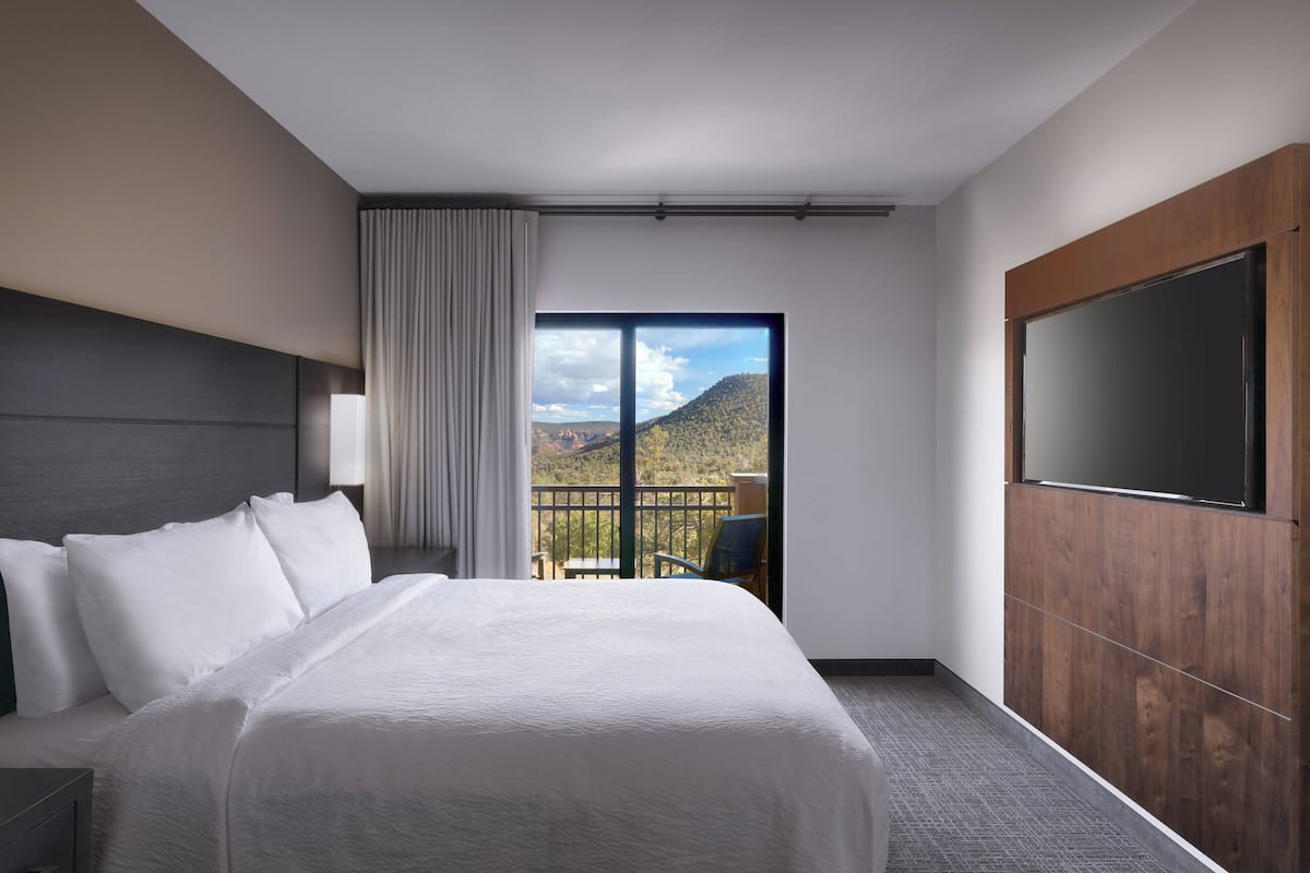 A hotel room with a large bed, a TV, and a balcony with a mountain view.