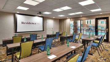 A conference room with multiple tables and chairs, a projector screen displaying "Residence Inn by Marriott", and a view of a pool through large windows.