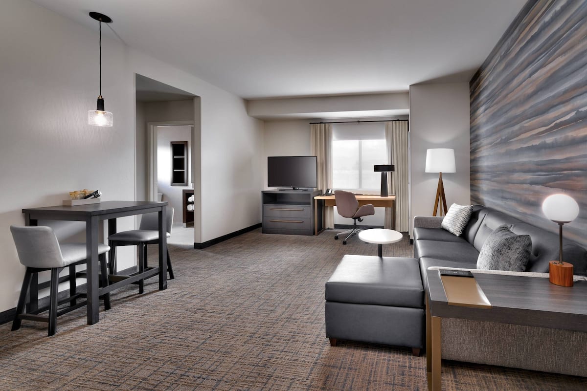 A modern hotel room with a dining area, a sofa, a TV, and a desk.