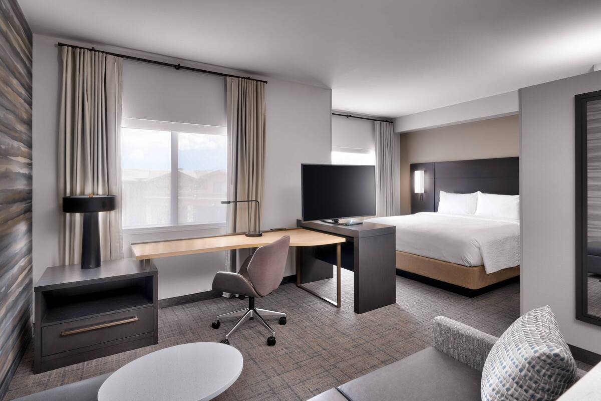 A modern hotel room with a bed, desk, chair, TV, and a view of the mountains.