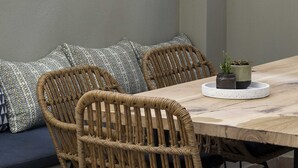 Een eetgedeelte met een houten tafel, rieten stoelen en gestreepte kussens.