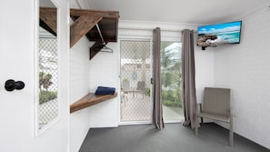 A room with a white brick wall, a TV mounted on the wall, a wooden shelf, a chair, and a sliding glass door leading to an outdoor area.