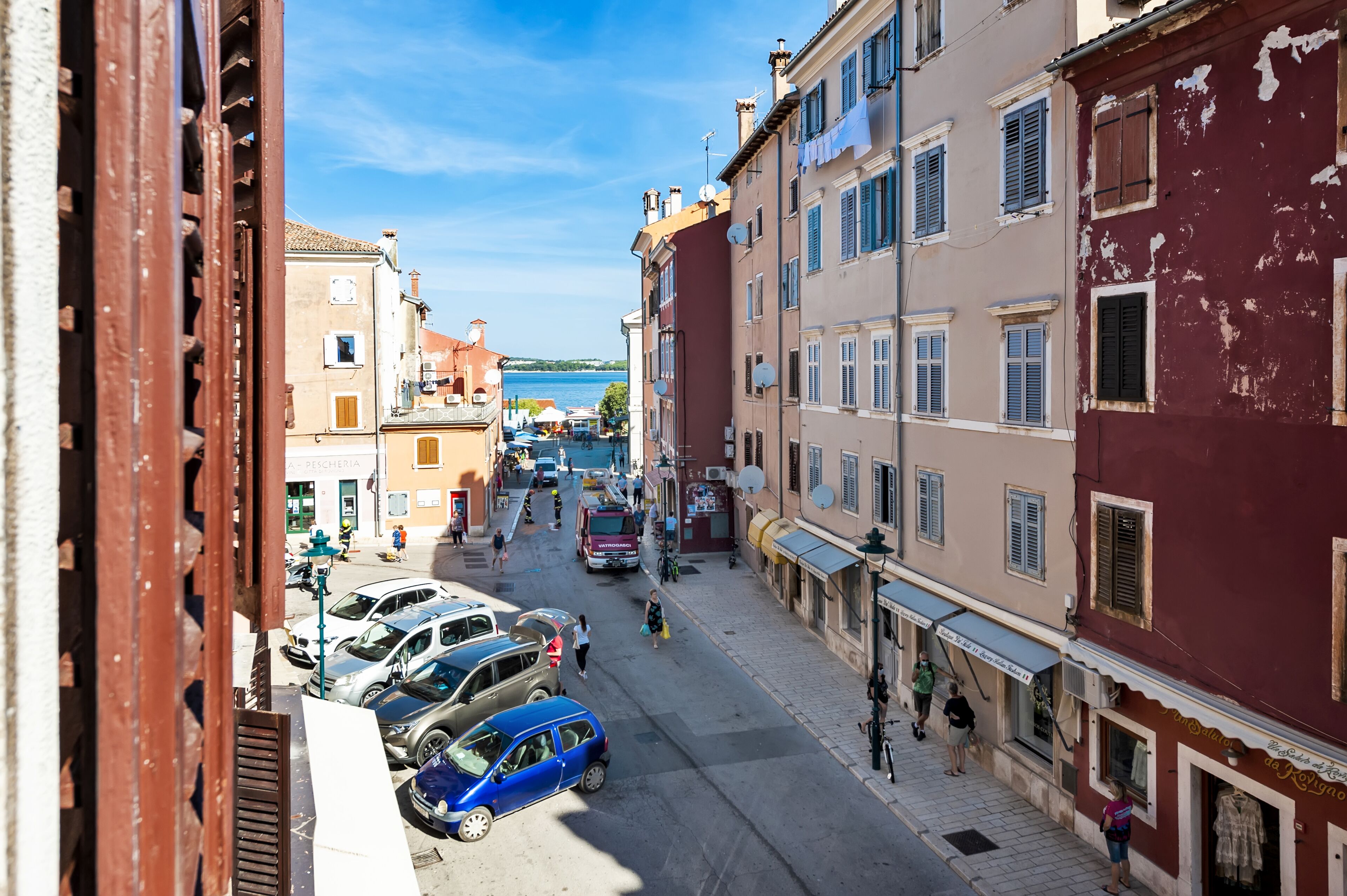 Una stretta via con auto parcheggiate e passanti.