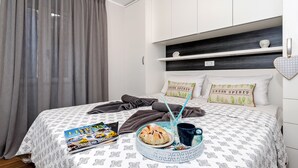 Una cama bien hecha con una colcha estampada, una bandeja con croissants, una revista y una taza.