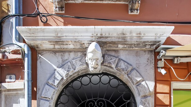 Una puerta doble marrón con un arco decorativo encima, una placa con el número 1670 y un escalón que lleva a la puerta.