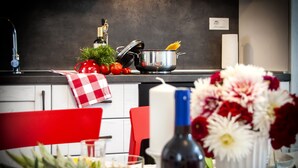 Una cocina con una toalla a cuadros roja y blanca, una olla de pasta, una botella de vino y un jarrón con flores sobre la encimera.