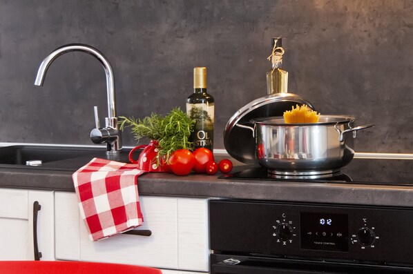 A kitchen with a modern faucet, a pot on the stove, fresh tomatoes, and a bottle of olive oil.