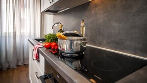 Una cocina moderna con estufa de acero inoxidable, una olla sobre la placa de inducción, tomates frescos y una botella de aceite de oliva.
