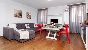 Una sala de estar moderna con un sofá gris, sillas rojas, una mesa de comedor con flores y un televisor.
