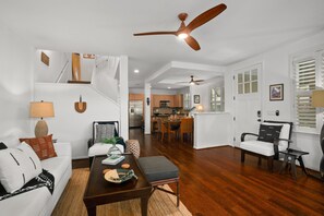 A spacious living area with a wooden floor, a dining table, a sofa, and a ceiling fan.