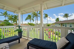 A covered outdoor area with a bench and a table, surrounded by white railings and palm trees.