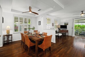 Un coin repas avec une table en bois et des chaises orange, un ventilateur de plafond et un téléviseur en arrière-plan.