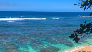 Une plage avec une eau turquoise et limpide, des rochers apparents et un rivage sablonneux.