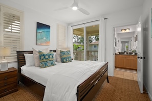 A bedroom with a bed, a nightstand, a ceiling fan, a painting, a sliding glass door, and a view of the outdoors.