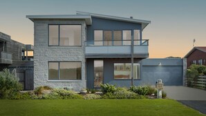 A modern two-story house with large windows, a stone facade, and a well-maintained lawn.