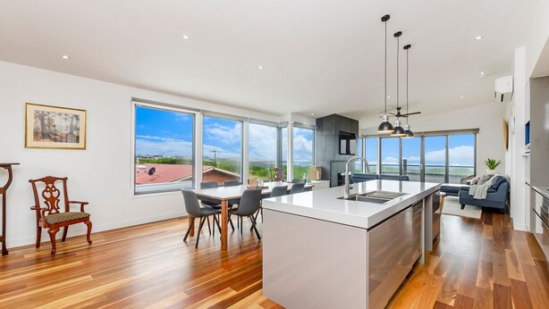 A modern kitchen with a large island, a dining area with chairs, and a view of the outdoors.