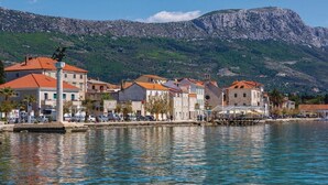 A coastal town with buildings along the waterfront, a pier, and a mountain in the background. - Studio Apartment with jaccuzzi (Kaštel Novi)