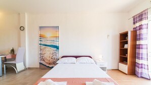 A hotel room with a bed, a desk, a chair, a bookshelf, and a painting of a beach scene. - Studio Apartment with jaccuzzi (Kaštel Novi)