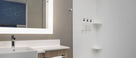 Un bagno moderno con uno specchio grande, un lavabo bianco, un portasciugamani e una cabina doccia.