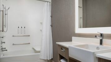 A modern bathroom with a bathtub, shower, and sink. There are handrails and a towel rack.
