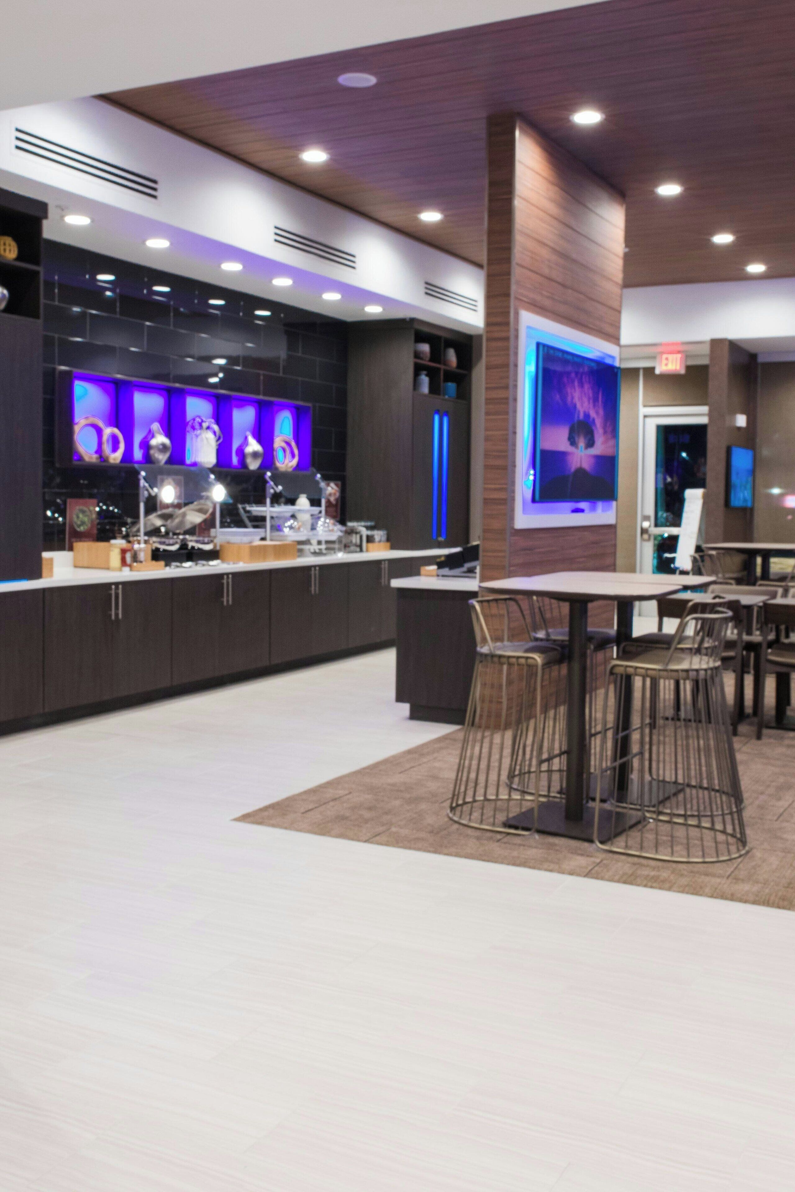 Un espace bar moderne doté d’un long comptoir, de nombreux sièges et d’un grand écran diffusant des images.