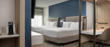 A hotel room with two beds, a desk, a chair, a coffee maker, and a TV.