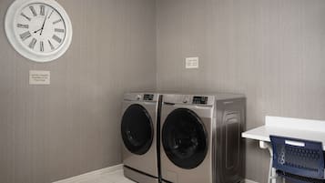 A laundry room with two front-loading washing machines, a wall-mounted clock, and a small table with a chair.