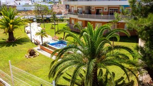 Un hôtel à plusieurs étages doté d’une piscine, de palmiers et d’un jardin clos.
