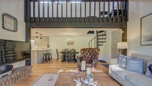 Ampla sala de estar com pé direito alto, escada, espaço para refeições e sofá com almofadas decorativas.
