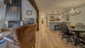 Uma cozinha moderna com ilha central, piso de madeira e área de jantar com uma cadeira de couro marrom e uma mesa de madeira.