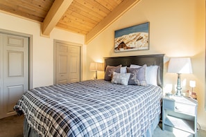 A bedroom with a large bed, two bedside tables with lamps, a headboard, and a painting of a snowy landscape.