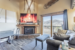 A living room with a fireplace, a television, and a large window offering a mountain view.