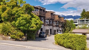 A multi-story building with a wooden balcony structure, surrounded by lush greenery and mountains in the background.