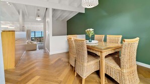 A dining area with a wooden table and wicker chairs, a green accent wall, and a view of the outdoors.