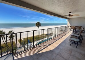 Un balcon avec vue sur la plage, des meubles d’extérieur et un ventilateur de plafond.
