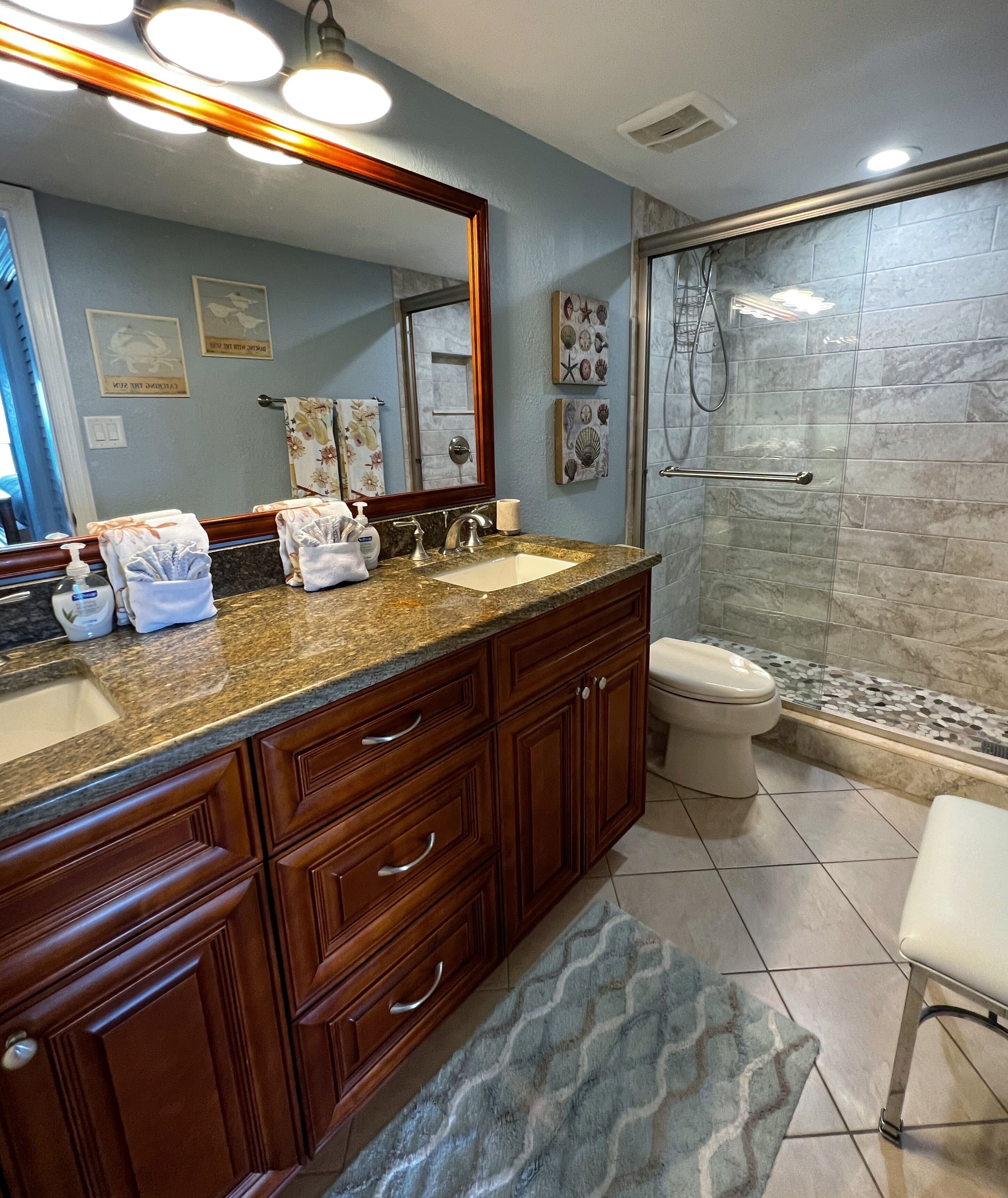 A bathroom with a granite countertop, wooden cabinets, a large mirror, a toilet, and a shower area.
