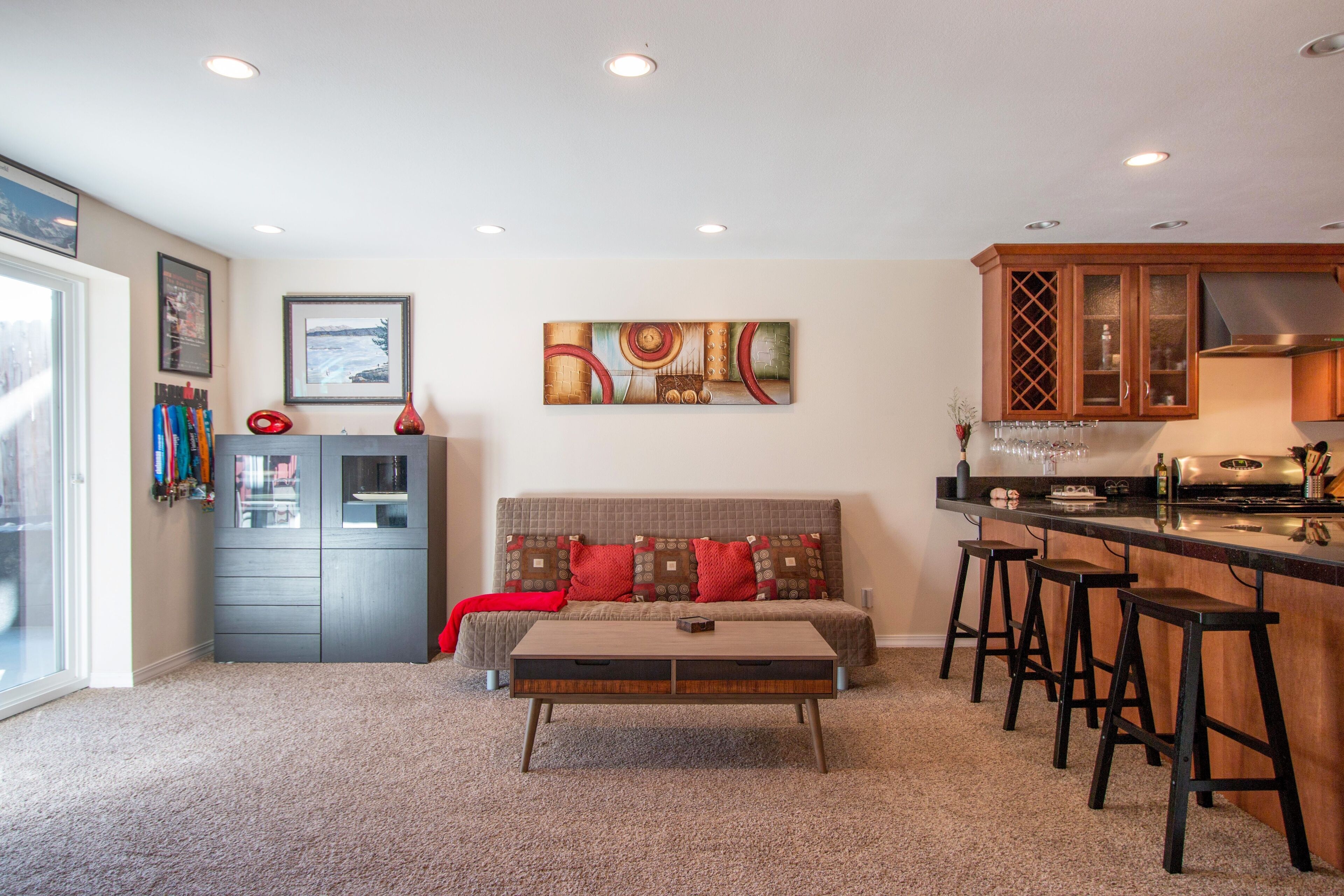 A compact living space with a sofa, ottoman, and bar stools. A kitchenette is visible with a stove and bar counter.