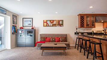 A compact living space with a sofa, ottoman, and bar stools. A kitchenette is visible with a stove and bar counter.