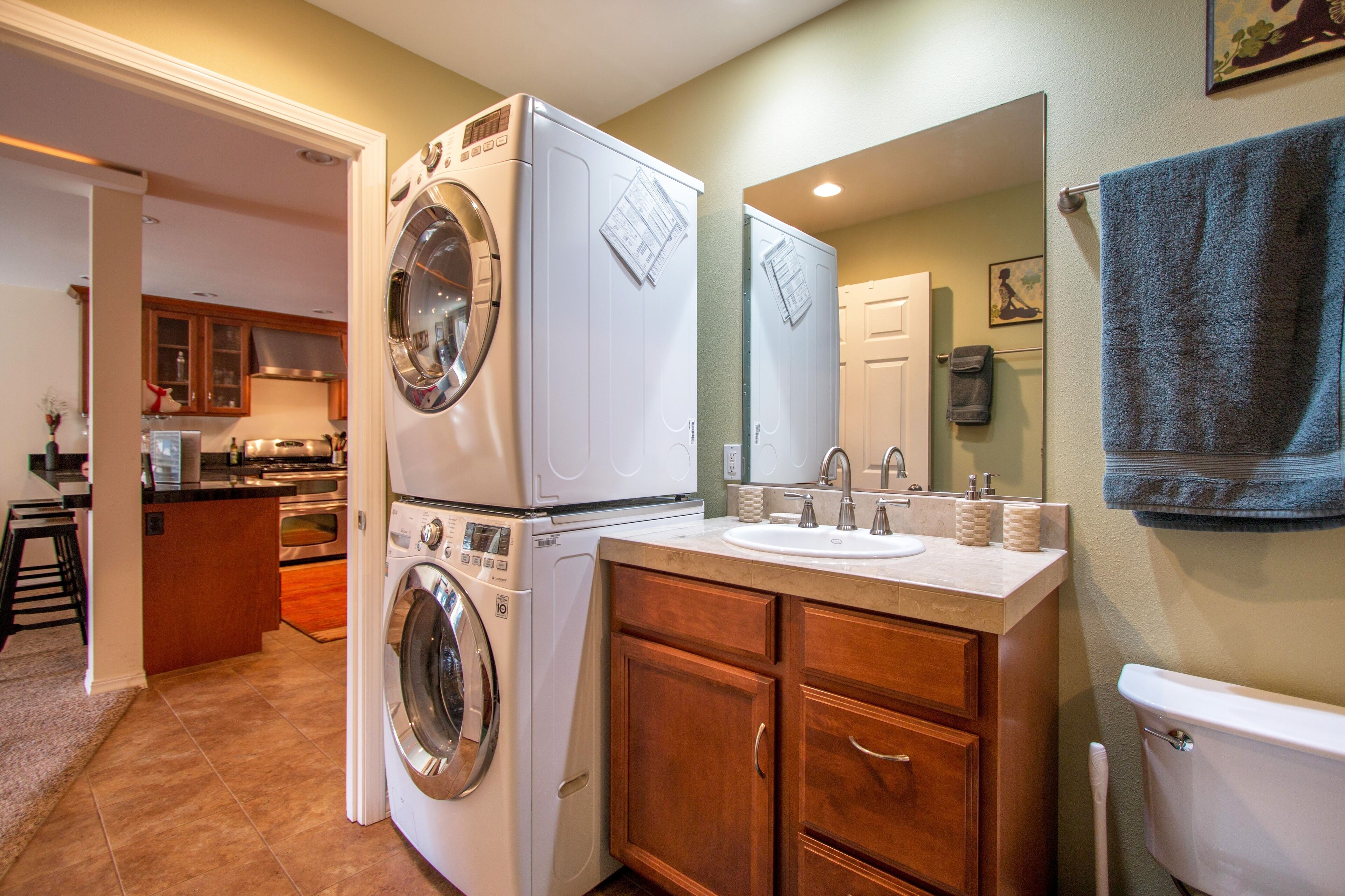 A laundry room with stacked washer and dryer, wooden cabinets, and a sink with a mirror above.