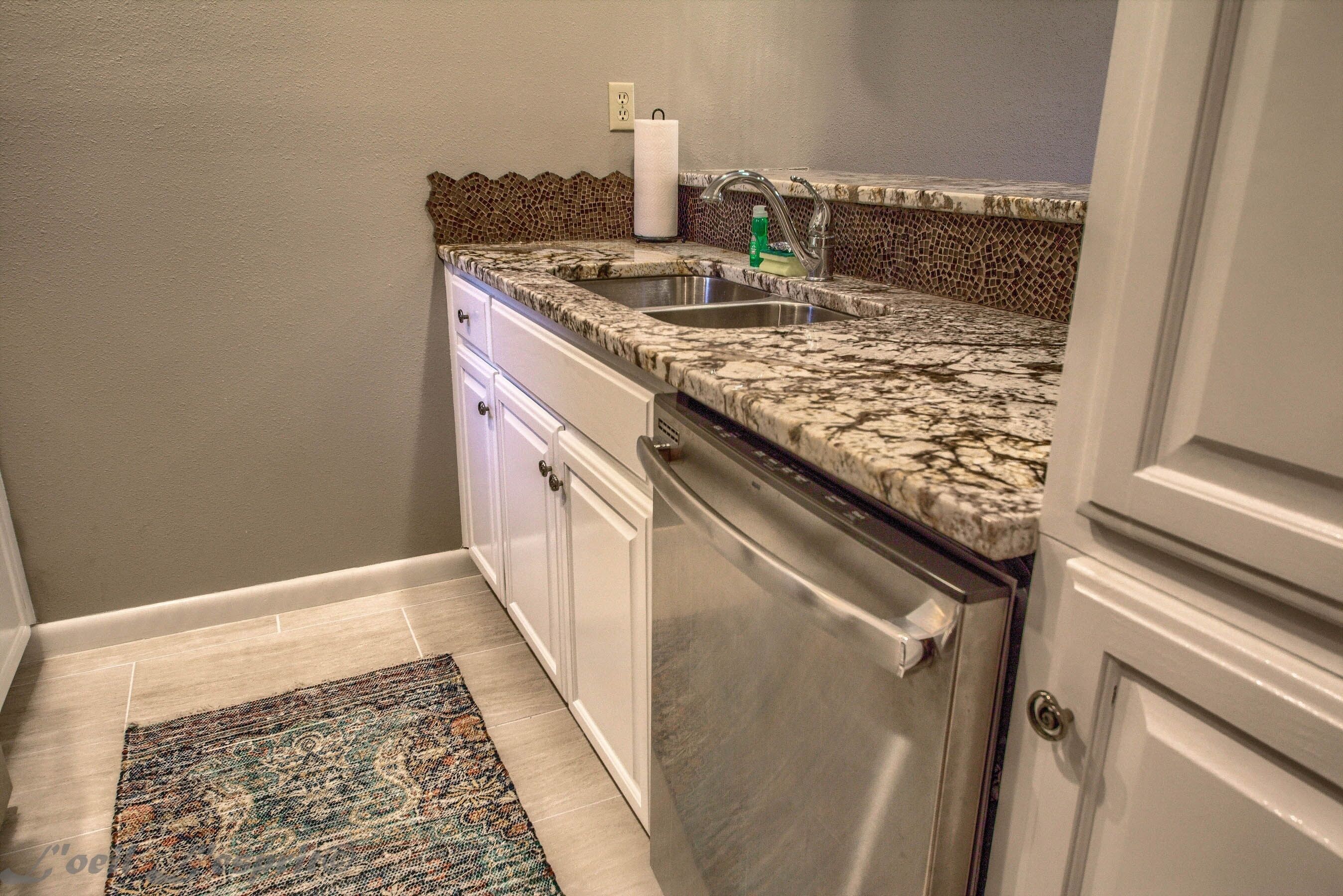 A compact kitchen with a granite countertop, stainless steel appliances, and a patterned backsplash.