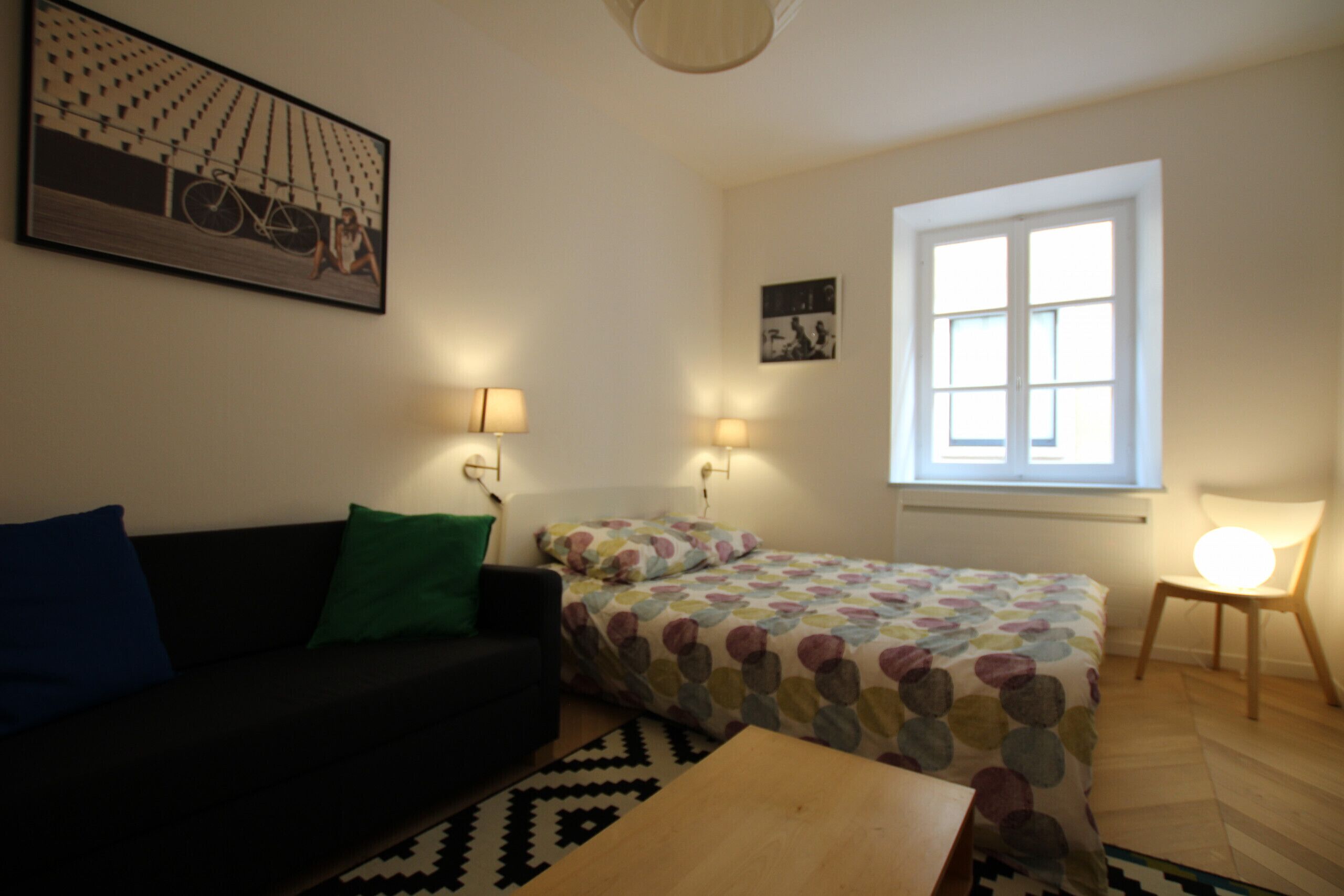 Ein Zimmer mit einem Bett, einem Schlafsofa, einem kleinen Tisch und einem Fenster.